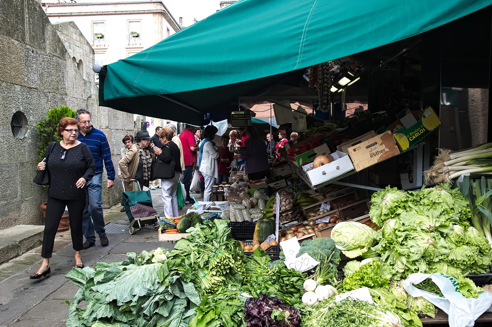 Puesto de verduras y hortalizas frescas con clientes en el Mercado de Abastos de Santiago de Compostela