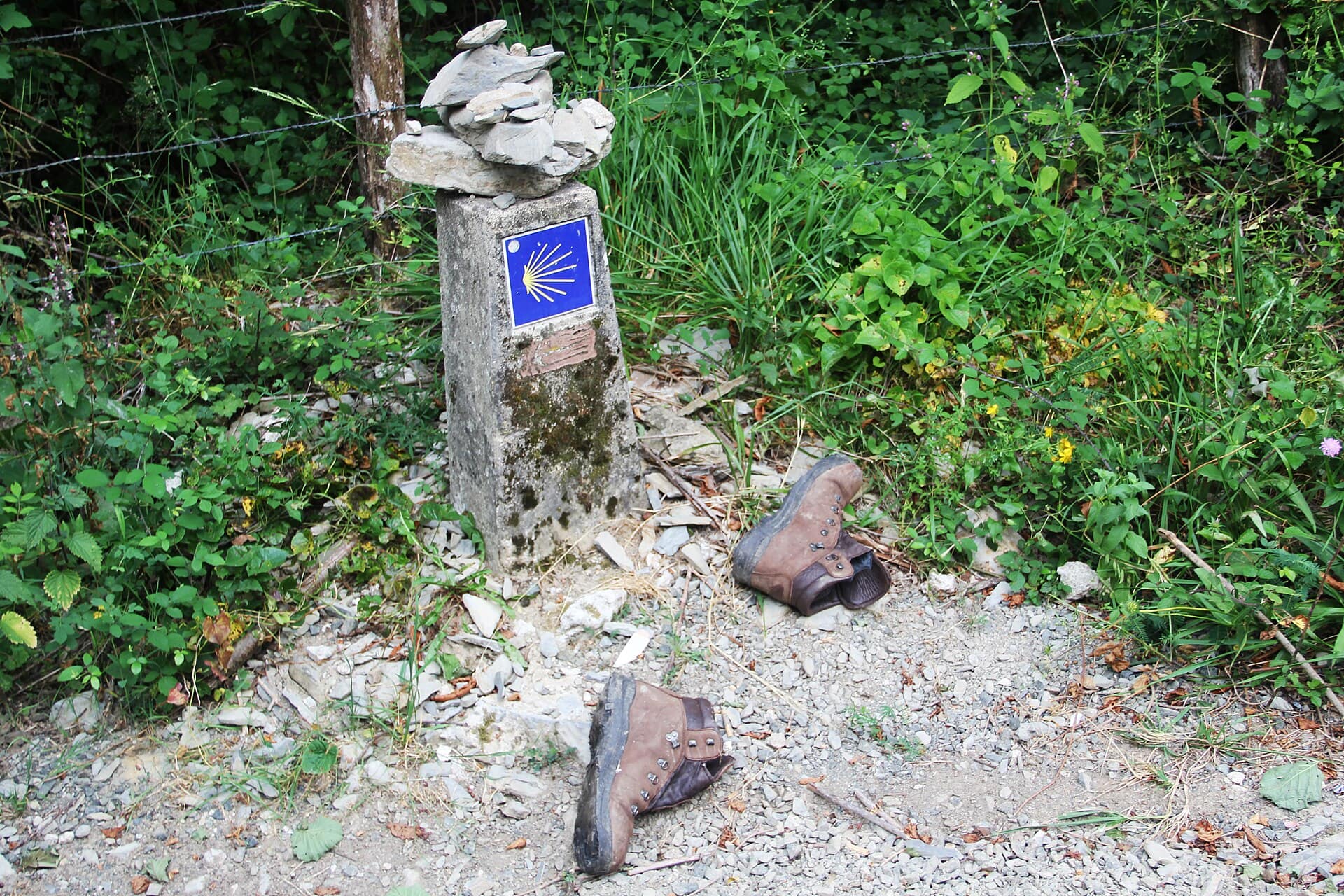 Mojón del Camino de Santiago con la concha amarilla junto a un par de botas de senderismo gastadas