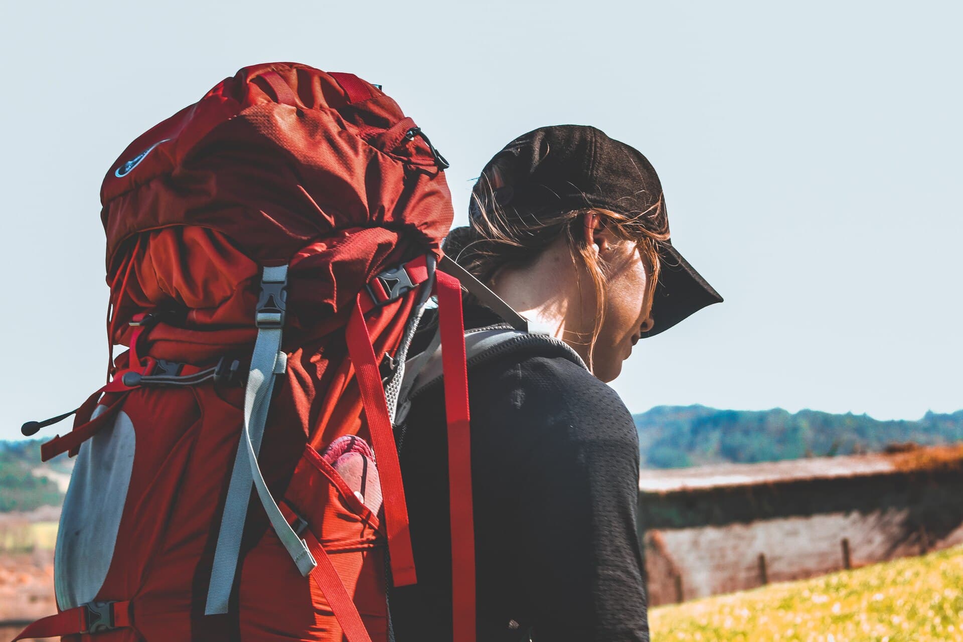 Peregrina con gorra y una gran mochila de trekking roja, caminando sola por el Camino de Santiago