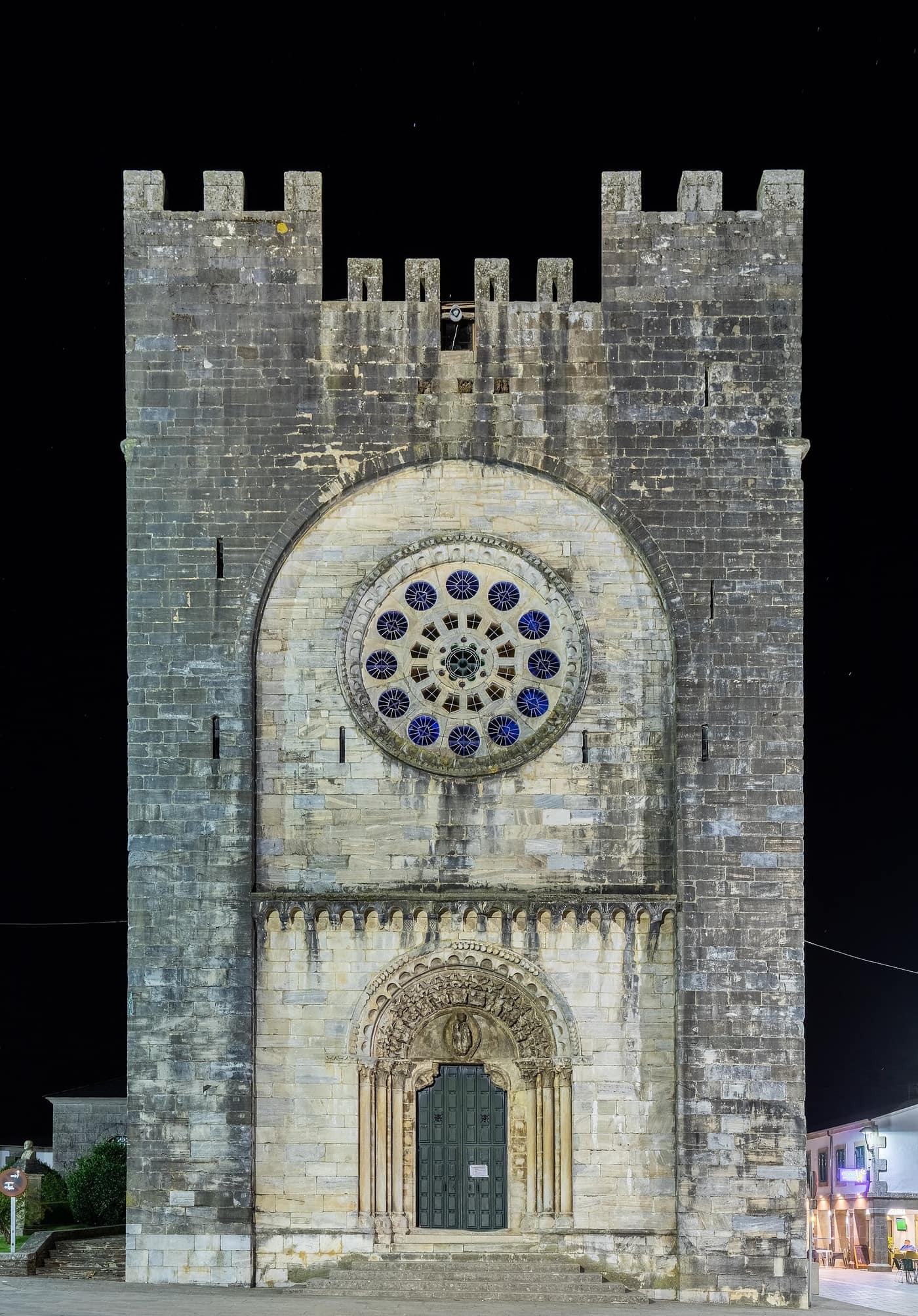 Fachada nocturna iluminada de la iglesia fortaleza de San Nicolás de Portomarín, con su rosetón románico, junto al Camino Francés