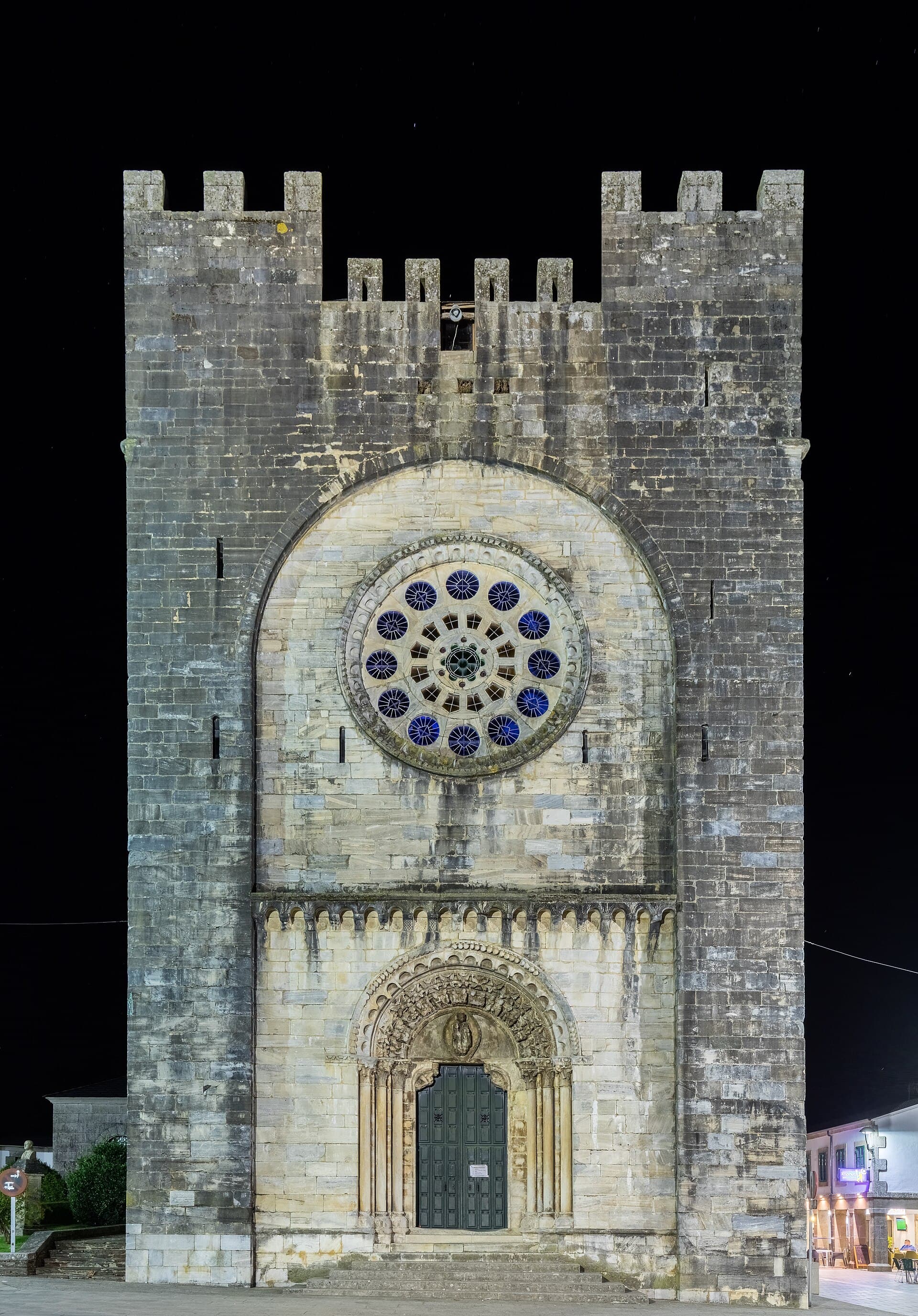 Fachada nocturna iluminada de la iglesia fortaleza de San Nicolás de Portomarín, con su rosetón románico, junto al Camino Francés